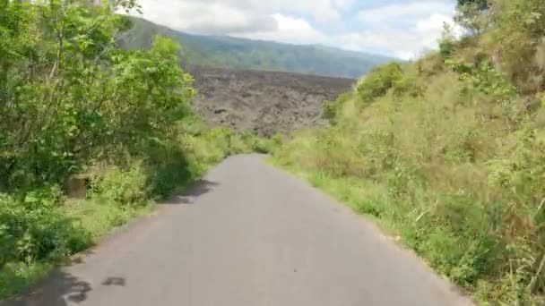 Pov person av en resenär som kör längs en vacker bergsbelagd väg med gröna växter mot en stor vulkan. En motorcykeltur genom underbara pittoreska platser. En solig dag. — Stockvideo