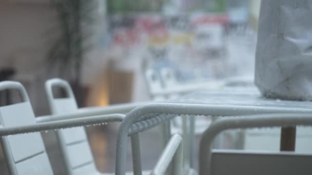 White tables and chairs of street restaurant in pouring rain on background of a wall with colored graffiti. Empty tables and chairs of closed cafe due to coronavirus pandemic and quarantine Cloudy — Stock videók