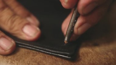 Yakın plan. Yetişkin çalışan elleri olan bir terzi siyah deri ceketli perçin altından demir yumrukla delik açar. Deri kaplı el yapımı, eski bir ustanın elleri. Ağır çekim. 4k.