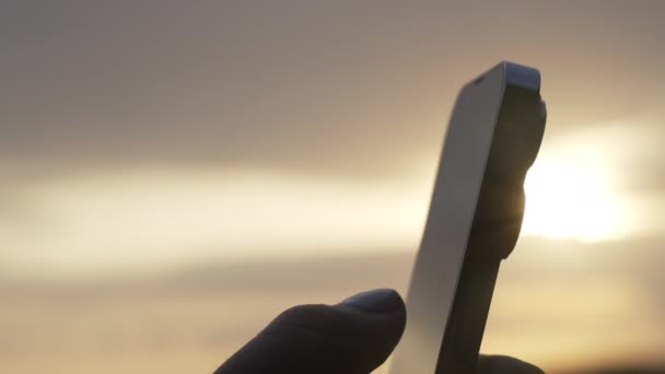 タッチスクリーンと2021年の現代的なファッショナブルな携帯電話に指で押す人。暖かい日没の背景に電話で非常に美しい人間の手。接近中だ。スローモーション. — ストック動画