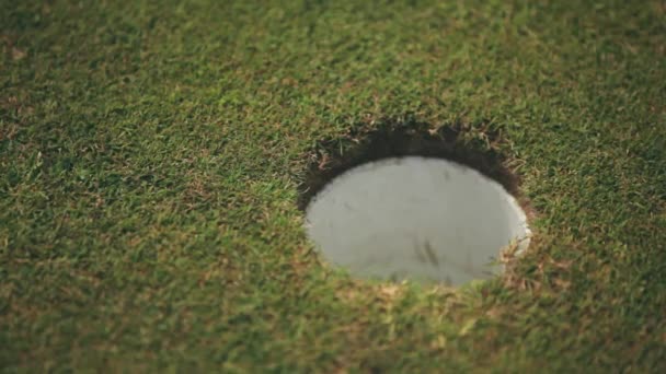 A white golf ball rolls past in holes on a golf course with green grass, close-up. Moment the ball misses and the white ball does not hit the hole. The moment of playing golf. A loss, a missed shot. — 图库视频影像