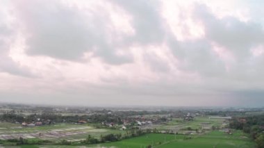 Gökyüzünden çekilen büyük gri bulutlarla birlikte yeşil tarlalar, evler ve sokaklar üzerinde pembe bir günbatımı gökyüzü. Bali Endonezya adasının kuş bakışı görüntüsü.