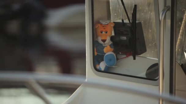 En närbild av kaptener stuga på båt och en plysch leksak i form av kaptener tiger ligger bakom glas, mot bakgrund av vackra sol bländning på vatten och bländning. En lugn avkopplande stund i viken. — Stockvideo