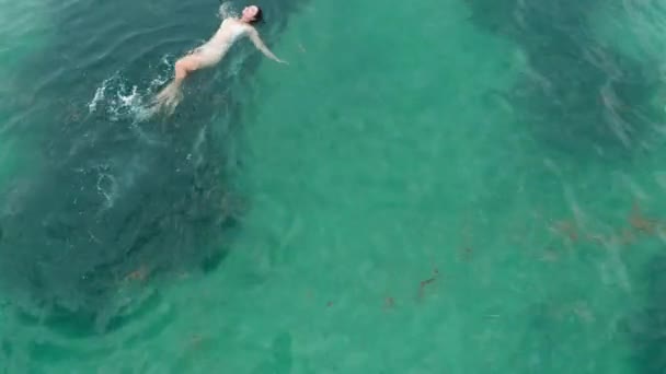 Imágenes aéreas de una chica asiática feliz en bikini blanco nadando en agua verde del océano con arrecife oscuro. Ejercicio deportivo pacífico y relajación en el cálido mar verde. Solo en la naturaleza salvaje. — Vídeos de Stock
