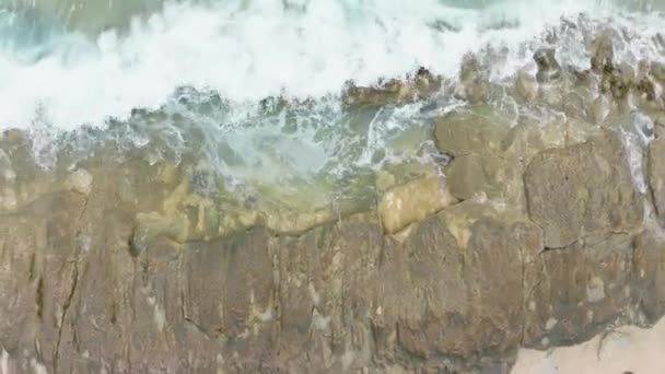 Cena aérea dramática com ondas verdes do oceano batendo em rochas marrons com espuma branca e salpicos. Imagens de drones de tiro superior de energia poderosa e natureza selvagem. Paisagem de praia com cores delicadas. — Vídeo de Stock