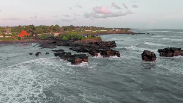 A beautiful aerial view of black rocks at ocean shore at golden hour. Tropical coast line panoramic footage at sunset. white sea foam crashing on dark reef in Bali island. — Stock Video