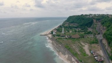 Güneşli bir günde kumsalın güzel sahil şeridine kuşbakışı bir manzara beyaz bir deniz feneri, yollar ve turist kulüpleri. Bali, Pandawa Sahili 'nin havadan manzarası. Endonezya 'da. Okyanus manzarası.