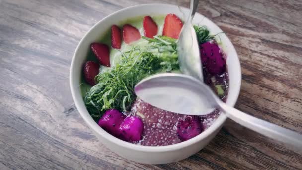 Ένα υπέροχο τροπικό μπολ smoothie με σπόρους chia, φρούτα δράκου, σπανάκι και φράουλες. Δύο κουτάλια βγάζουν κομμάτια από φρούτα δράκου από νόστιμο υγιεινό πρωινό με γιαούρτι και φρούτα. — Αρχείο Βίντεο