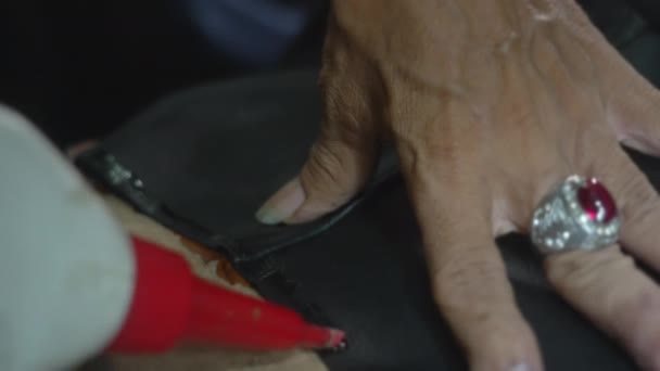 Jimat anonim tangan mengaplikasikan lem pada permukaan kulit jaket. Menggantungkan lengan dari barang kulit asli selama proses pembuatan jahit. Membuat pakaian kustom close-up. — Stok Video