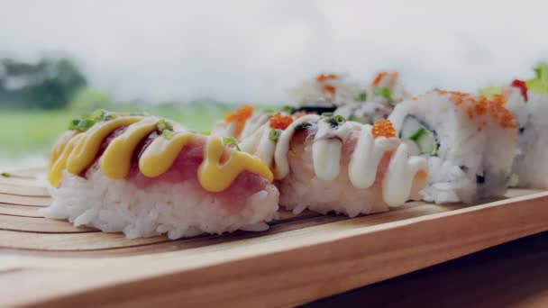 Крупный план человека, берущего суши с лососем из деревянной стойки. Вкусные суши в японском ресторане с прекрасным видом через панорамное окно зеленых рисовых полей и неба — стоковое видео