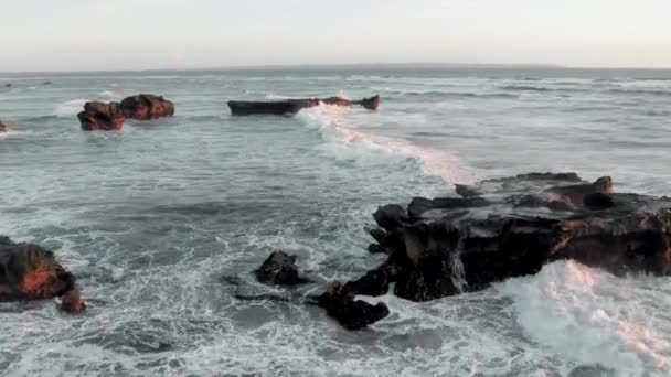 En vacker flygning över svarta klippor på havet i gyllene timme. Panoramabilder av kustlinje, oceanrev vid solnedgången. En stark vit våg och havsskum bryter på mörka rev på ön Bali. — Stockvideo