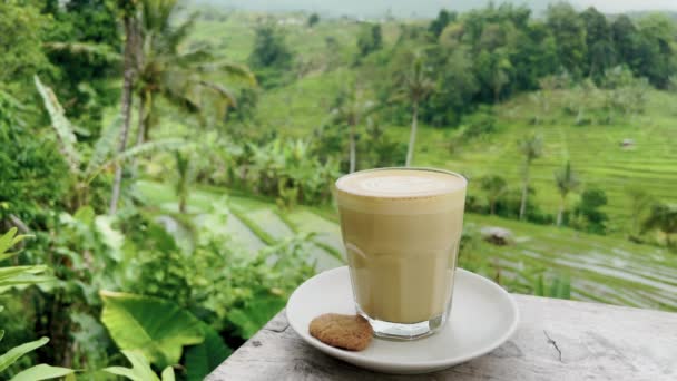 El hombre se sumerge en una deliciosa galleta en una taza de café contra el telón de fondo de pintorescas terrazas de arroz. El turista disfruta de vistas a las plantaciones de arroz y al café blanco plano. plantaciones de arroz en las montañas de — Vídeo de stock