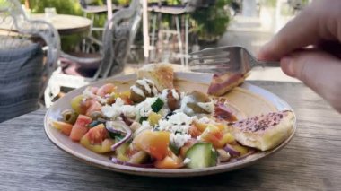 Açık havada güneşli bir yazlık kafede nohut köftesi ve sebze yiyen bir adam. İnsan falafel kesmek için çatal kullanır. Palmiye ağaçlarının gölgesinde sağlıklı ve lezzetli bir öğle yemeği. Yakın plan..