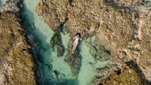흰 비키니를 입은 여성 이 바다의 자연적 인 산호초 위에 누워 휴대폰으로 이야기하는 장면입니다. 손에 전화기를 들고 사업에 관해 이야기하고 야생계에서 상의 하는 예쁜 소녀의 사진 — 비디오
