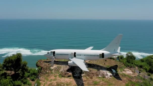 절벽 끝에 있는 낡은 흰 비행기 가 바다 근처의 녹색 열대 낙원에 있습니다. 발리 섬에 버려진 비행기 가 해변에서 파노라마처럼 바다를 조망하고 있습니다. 공중에서 본 항공로 와해 안 위 의언 덕들 — 비디오
