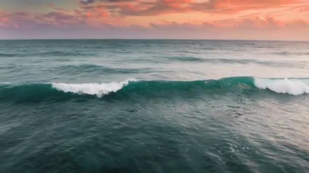 Imágenes aéreas de hermosas olas verdes rompiendo mientras rodan a la orilla del mar. Imágenes de drones de energía oceánica en el hermoso atardecer rosa anaranjado en la isla Bali. Lavado blanco de espuma de mar en el océano Índico — Vídeo de stock