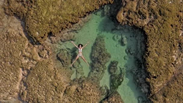 흰 비키니를 입은 여성 이 바다의 자연적 인 산호초에 누워 있는 장면입니다. 팔 과 다리를 뻗고 야생계에서 별 모양으로 뻗어 누워 있는 예쁜 소녀 의 드론 사진. — 비디오