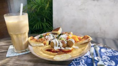 Açık bir kafede nefis bir sütlü kahve içerken nefis falafel ve humus tabağı, pide ekmeği ve sebzeyle birlikte. Palmiye ağaçlarının gölgesinde sağlıklı ve lezzetli bir öğle yemeği. Güneşli bir gün.