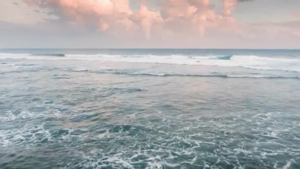Letecký pohled na zelené vlny, které se lámou na mořský břeh. Záběry bezpilotního letounu letícího nad oceánem při krásném oranžově růžovém západu slunce na ostrově Bali. Bílá záplava mořské pěny v Indickém oceánu. — Stock video
