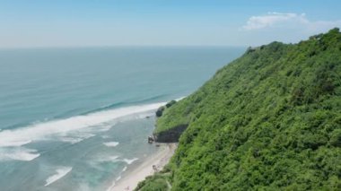 Yeşil yamaçlı tropikal bir adanın cennet manzarasındaki bir dron 'dan güzel bir manzara, beyaz kumlu bir plaj ve okyanustan gelen büyük dalgalar. Bali adasının havadan manzarası. 4k