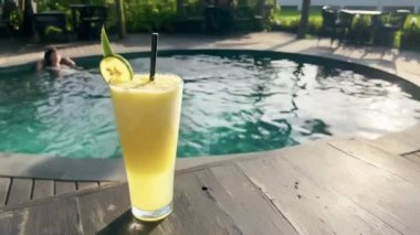 Güzel bir teras restoranında limon dilimli nefis tropikal meyve suyu yüzme havuzunda güneş ışığı parlaklığı yaratır. Lezzetli bir ananas suyu. Bir kızın havuzda dinlendiği..