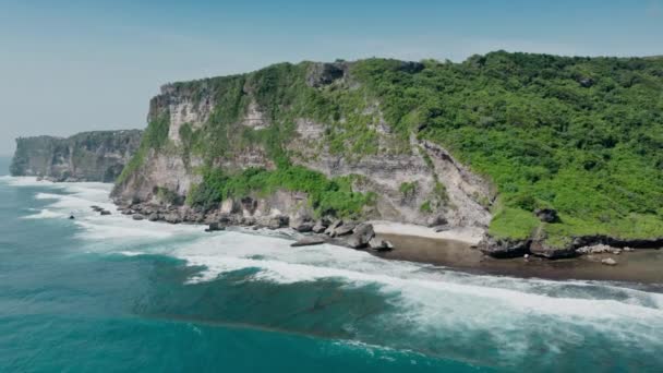 Increíble vista aérea de altos acantilados con árboles verdes y arbustos sobre el rugiente océano. Imágenes dinámicas del helicóptero de la costa del océano acanalada con piedras de lavado de espuma de mar blanca salpicaduras. — Vídeo de stock