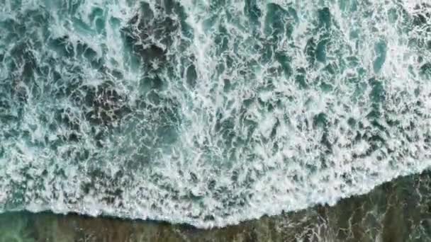 Statische Luftaufnahmen von braunen Riffen mit azurblauem Wasser, das von Wellen bedeckt ist, die in weißes Meerschaumwasser krachen. Kopieraufnahmen von Gezeitenbrandung, die felsige Meeresküsten unterspült. Drohnenschuss aus Stein und Wasser — Stockvideo