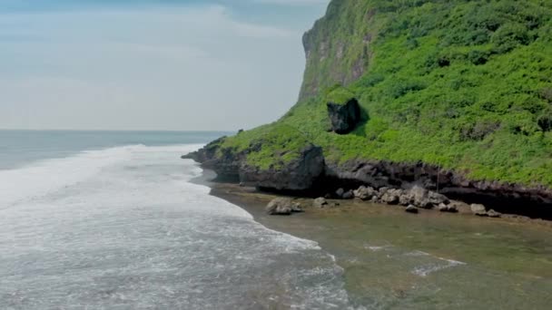 Incredibile vista aerea di alte scogliere con alberi verdi e cespugli sopra ruggente oceano. Filmato dinamico dell'elicottero della costa oceanica rocciosa con schizzi di pietre lavanti bianche di schiuma marina. Isola di Bali. — Video Stock