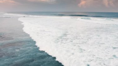 Deniz kıyısına yuvarlanırken kırılan yeşil dalgaların durağan hava görüntüsü. Bali Adası 'ndaki portakal rengi pembe günbatımında okyanus üzerinde dron görüntüsü. Hint okyanusunda beyaz deniz köpüğü..