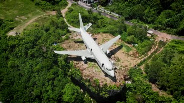 Biały samolot na brunatny ziemia w zielony tropikalny krzak. Widok z góry na opuszczony samolot w lesie z zakręconą drogą. Widok z lotu ptaka i wzgórz oraz zieleń. — Wideo stockowe