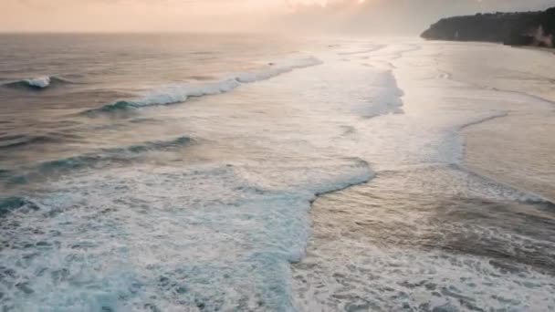 Коли вони котяться до берега моря, перед ними відкривається вигляд велетенських хвиль. Кадри дрона швидко літають над океанською енергією на прекрасному помаранчевому рожевому заході сонця на острові Балі. Біла мийка морської піни в Індійському океані.. — стокове відео