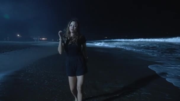 Een vrouwelijke vakantieganger dansend op een nachtstrand in oceaangolven. Moderne dans in blauw licht van een lamp in de buurt van de zee kam door een jonge vrouw op vakantie. gelukkig en gratis meisje na partij bewegen met muziek. — Stockvideo