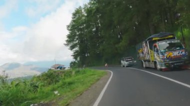 Kintamani, Bali, Endonezya - 10 Aralık 2021: Volkan ve dağların muhteşem manzarası ile dolambaçlı dağ yolunda araba süren bir kişi. Endonezya 'nın dağ yılanı. Film tahıl dokusu