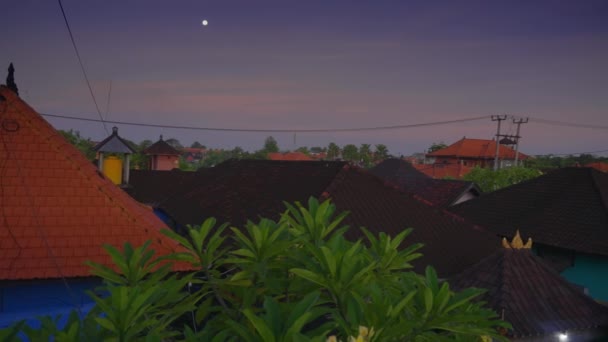 Amanecer paisaje urbano de la localidad en la isla de Bali en la luz suave. Cámara sartenes sobre hermosos techos de casas con azulejos nacionales de color naranja y pequeños templos contra el fondo de grandes volcanes y el cielo — Vídeos de Stock