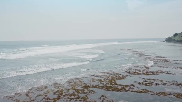 Letecký let velkých oceánských vln, které se za přílivu rozbíhají do bílé pěny na kamenném útesu. Pobřeží tropického ostrova s bílým pískem a velkými skalami. Pohled na Bali ostrov drone. — Stock video