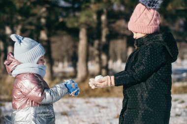 Karlı bir parkta kış yürüyüşüne çıkmış farklı yaşlarda iki kız kardeş.