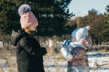 Karlı bir parkta kış yürüyüşüne çıkmış farklı yaşlarda iki kız kardeş.