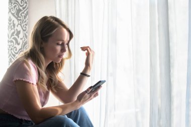 Üzgün güzel kız, evde telefona bakıyor.