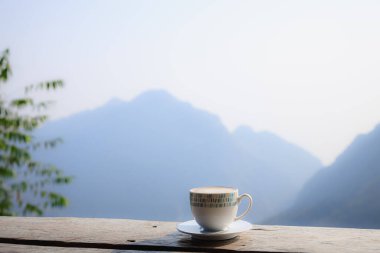 Sıcak kahve cappuccino beyaz fincanda ahşap terasta güzel manzaralı sabah manzarası arka planında phahee doi chiang rai Thailand 'da 