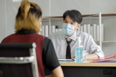 İşteki güvenli iletişim ve COVid-19 karantinası sırasındaki sosyal mesafe. Tayland 'da meslektaşlar koruyucu cam ve yüz maskesi ile konuşur. 