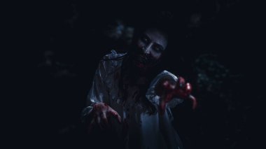 Beyaz gelinlik giymiş Asyalı genç bir kadının portresi hayalet ya da yüzünde zombi kanı, arka planda karanlık sahne filmi olan korku filmi, gece sahnesi konseptinde festival Cadılar Bayramı özel konsepti. 