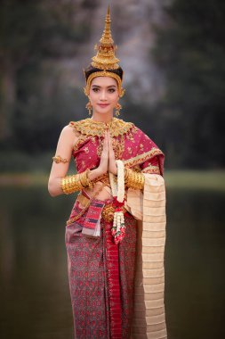 Taylandlı geleneksel elbise, kırmızı takılar içinde Thai modeli. Bahçe nehrinde ve dağ arka planında akşam vakti saygı ve gülümseme göstermek için hoş geldiniz.
