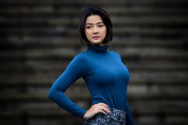 çekici ve güzel Asyalı kadın moda portresi mavi uzun kollu tişört ve siyah taş arka plan 