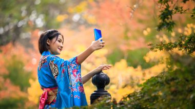 Japon mavi kimonosu giyen Asyalı genç bir kadının portresi Japonya 'nın sonbahar sezonunda parkta akıllı telefon ile selfie çekiliyor.