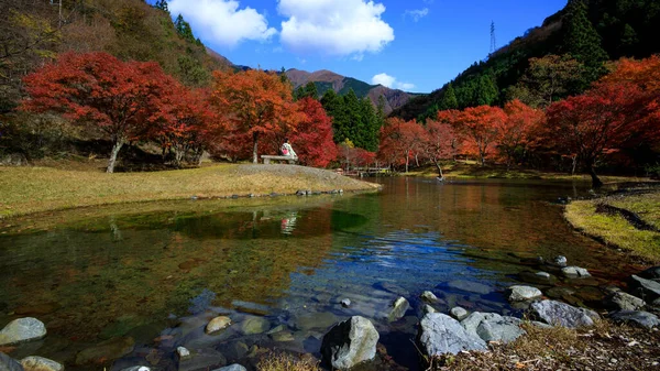 紅葉シーズンと着物を着た観光客が川公園の木製のテーブルの上に座っている日本語と青空の背景を持つ山 — ストック写真