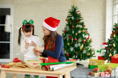 Asyalı anne ve kızı evdeki Noel ağacı etkinliklerinde birbirlerine yardım ediyorlar.