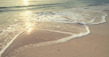 Uzun pozlama, kumlu sahili ve deniz dalgası beyaz baloncuklarını gündoğumu arka plan klasik resim tarzıyla çeker.  