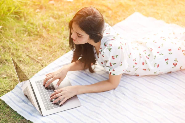 美丽的亚洲自由职业女性躺在花园里 躺在笔记本电脑上 做着轻松的工作 还有从家里的观念出发 在阳光下做着背景工作 — 图库照片