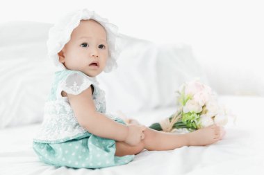 Taylandlı bebek beyaz yatakta dinleniyor ve gül çiçeği ön planda klasik tarz seçici odaklanıyor.