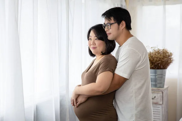 pregnant woman and her husband asia happy smiling while spending time together in the white bedroom and window light background baby love care concept